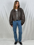 Frau in brauner Lederjacke, blauer Jeans und schwarzen Stiefeln vor weißem Hintergrund. Modetrend, lässiger Stil, Damenbekleidung.