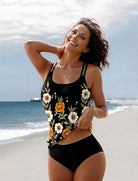 Frau am Strand in einem floralen Tankini-Set, schwarz mit gelben und weißen Blumen. Perfekt für Sommermode, Strandbekleidung, Bademode.