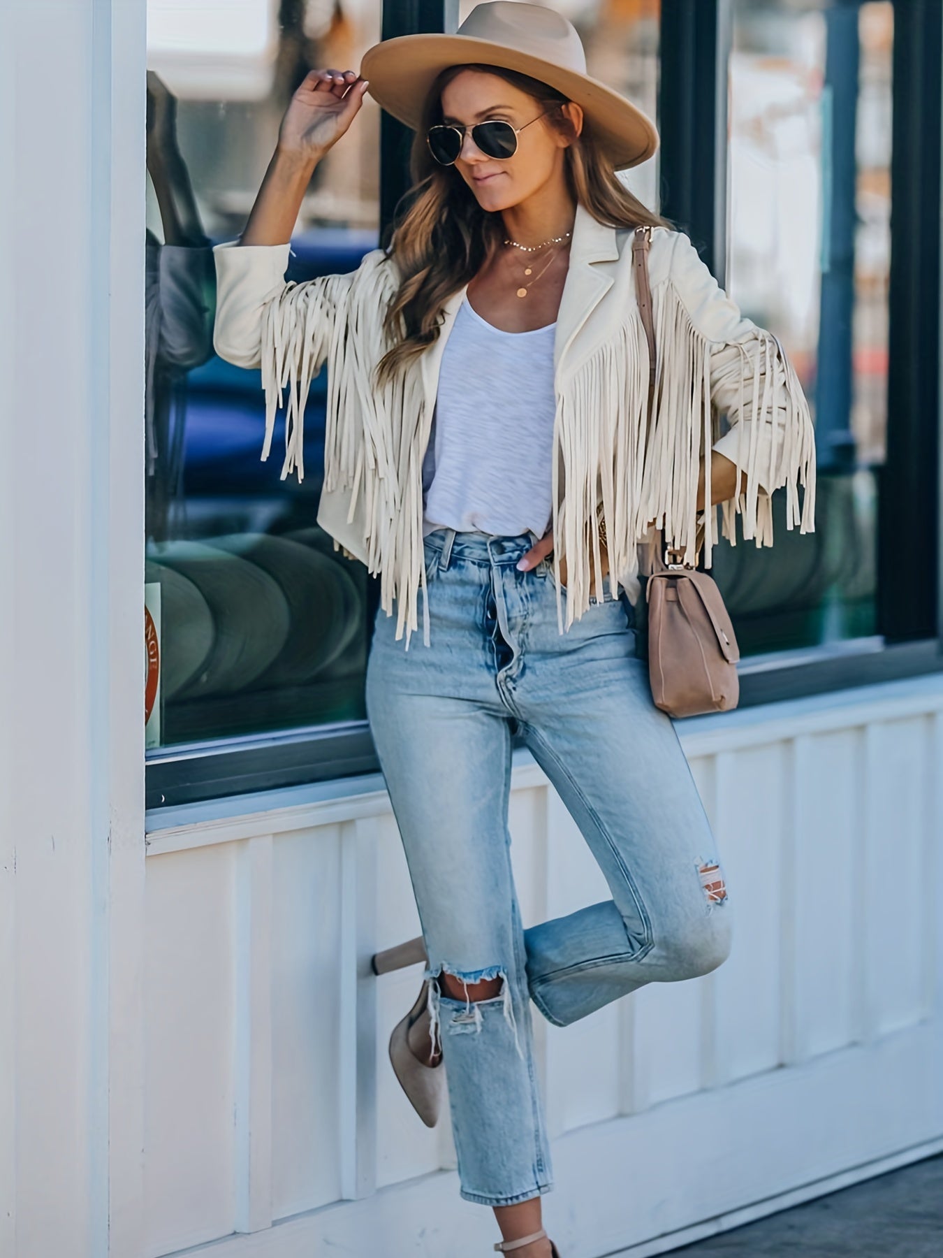 Frau in modischer Fransenjacke, zerrissenen Jeans und Sonnenbrille. Trendige Streetwear, lässiger Boho-Stil, ideal für urbane Mode-Looks.
