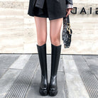 Damen tragen schwarze kniehohe Stiefel, kombiniert mit einem eleganten Rock und einer Designer-Handtasche. Perfekt für modische Herbst-Looks.