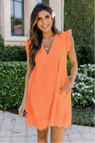 Frau in orangefarbenem Sommerkleid mit Rüschenärmeln, V-Ausschnitt und Blumendetail im Haar, steht vor grünem Garten. Perfekt für Sommermode.