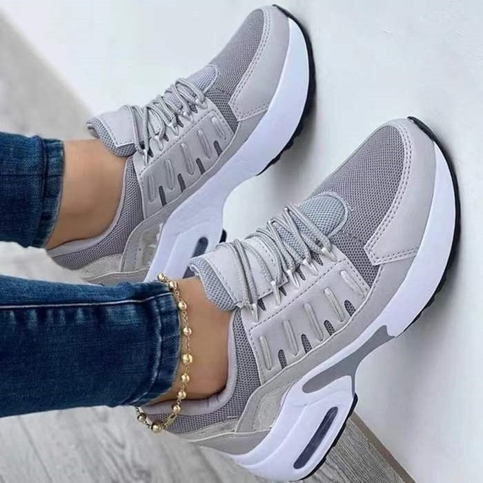 Graue Damen-Sneaker mit weißer Sohle, atmungsaktivem Mesh-Obermaterial und modischem Design. Perfekt für Sport und Freizeit.