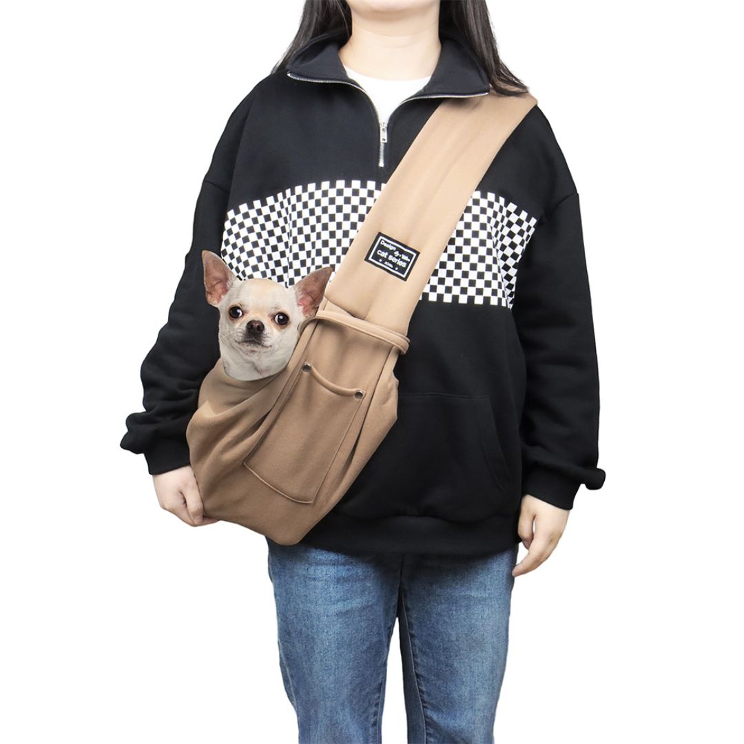 Person mit schwarzem Pullover und karierter Musterung trägt eine beige Hundetragetasche mit kleinem Hund. Perfekt für Haustiertransport, stilvoll und praktisch.