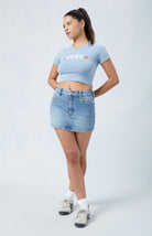 Frau in blauem Crop-Top und Jeansrock, lässiger Look, weiße Sneakers, modisch, urbaner Stil, Freizeitkleidung, trendige Damenmode.