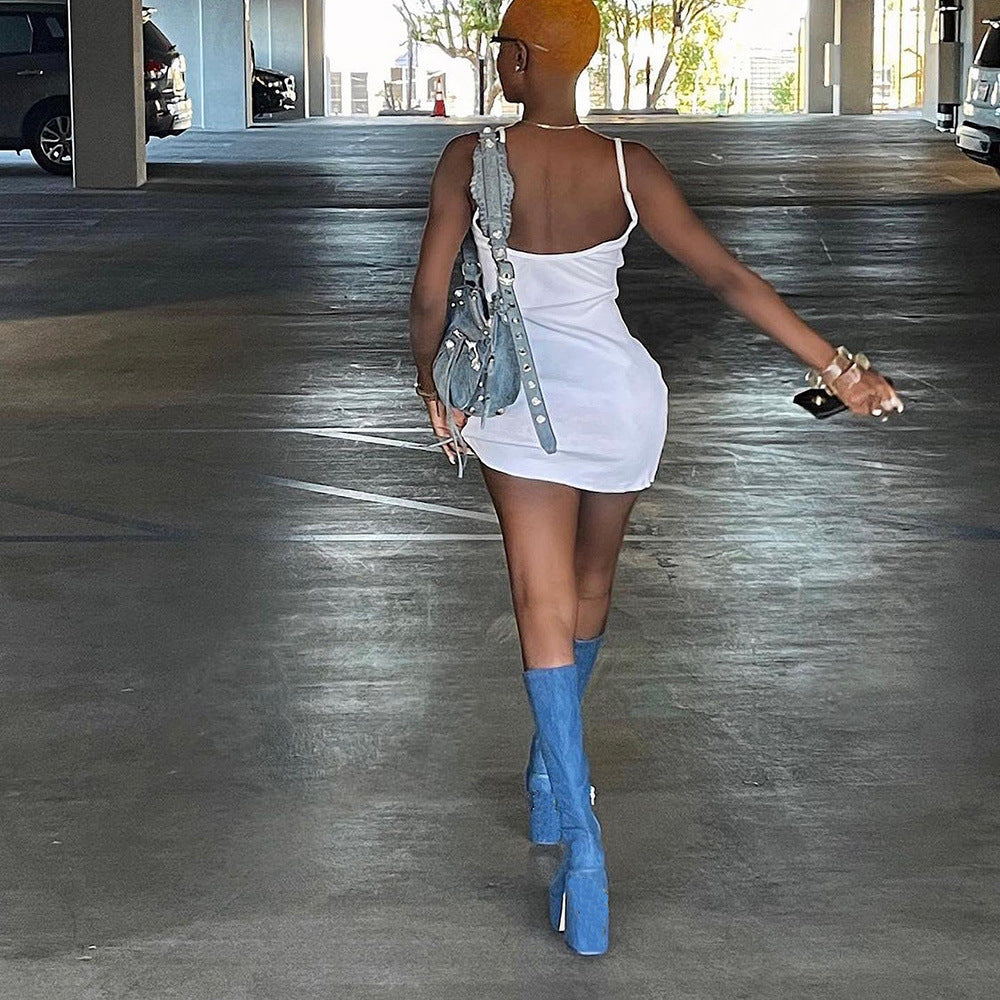 Frau in weißem Minikleid und blauen Stiefeln, trägt eine graue Handtasche, geht durch Parkhaus. Mode, Streetstyle, Sommeroutfit, urbaner Look.