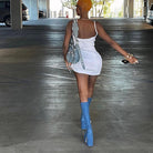 Frau in weißem Minikleid und blauen Stiefeln, trägt eine graue Handtasche, geht durch Parkhaus. Mode, Streetstyle, Sommeroutfit, urbaner Look.