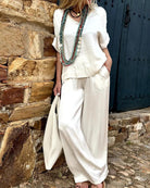 Elegantes Damen-Outfit in Weiß, bestehend aus lockerer Bluse und Hose, ergänzt durch lange Halsketten. Perfekt für Sommermode und Freizeitlook.