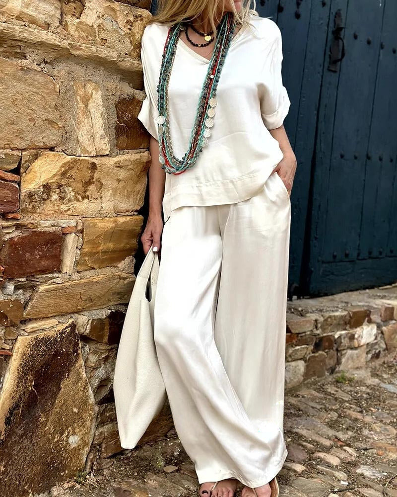 Elegantes Damen-Outfit in Weiß, bestehend aus lockerer Bluse und Hose, ergänzt durch lange Halsketten. Perfekt für Sommermode und Freizeitlook.