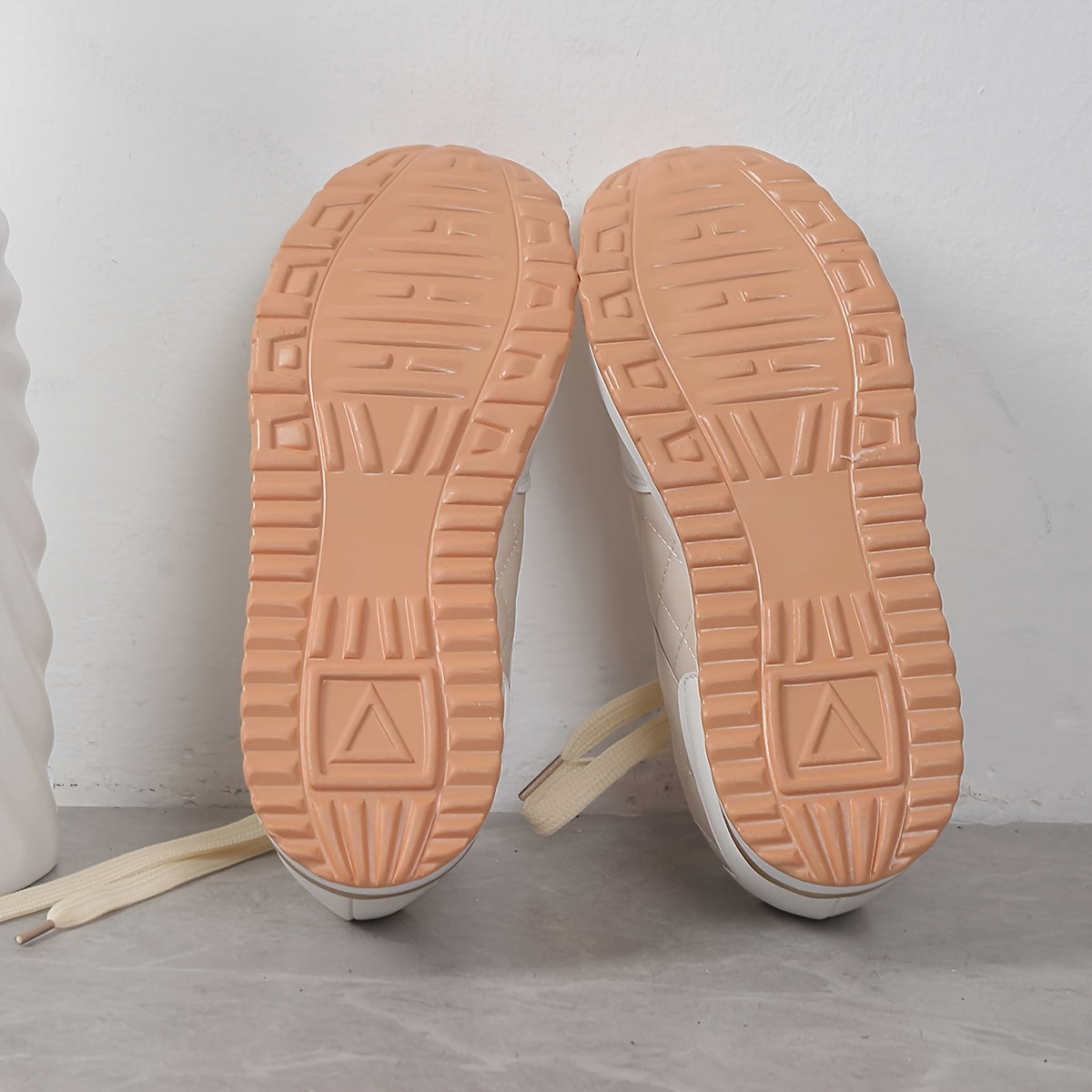Beige Sneaker-Sohlen mit rutschfestem Profil auf grauem Hintergrund. Ideal für Mode, Komfort und Alltag. Hochwertige Turnschuhe für Damen und Herren.