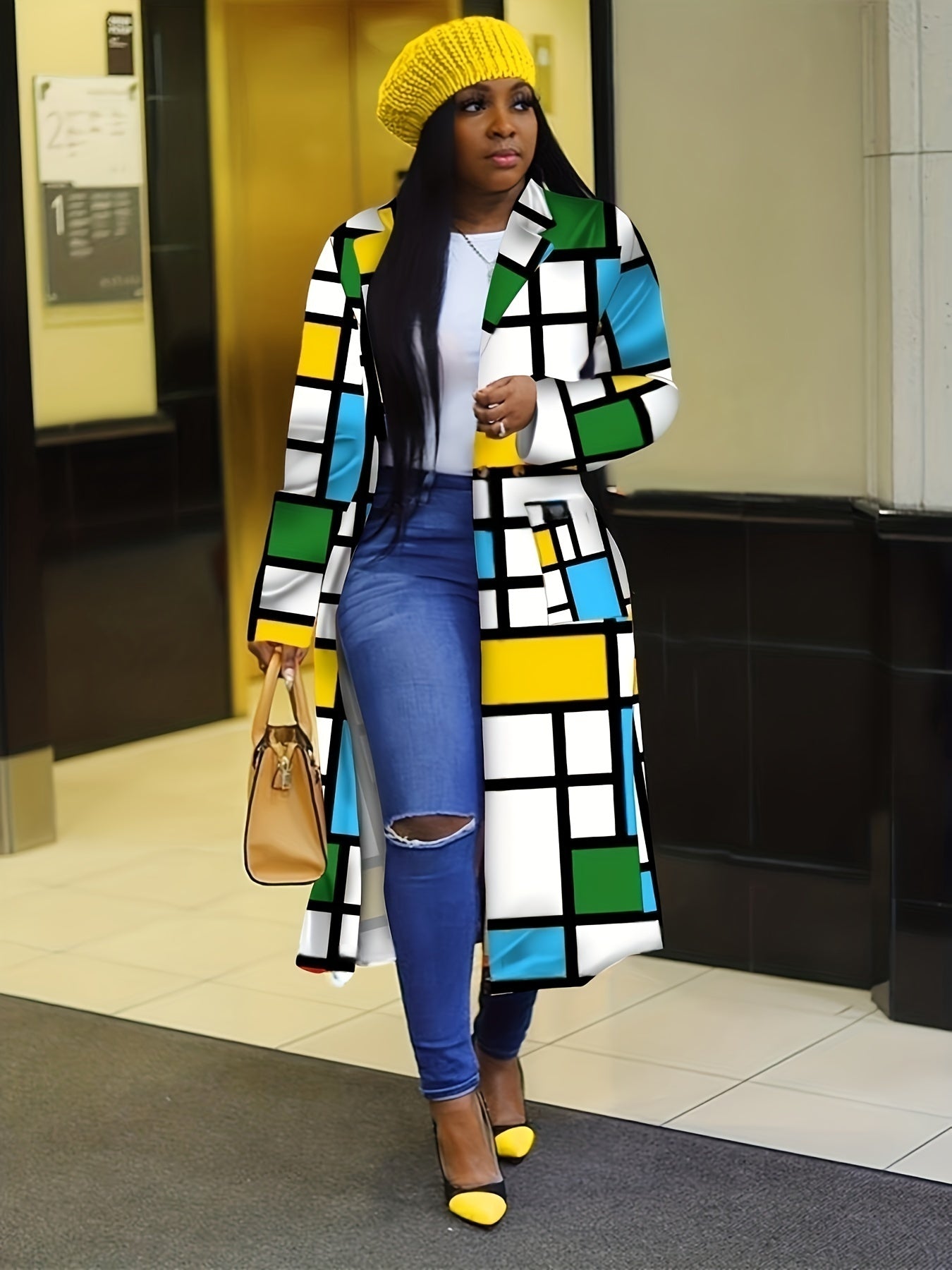 Frau in modernem, farbenfrohem Mantel mit geometrischem Muster, gelber Mütze und Pumps. Modetrend, Streetstyle, Herbstmode, Damenbekleidung.
