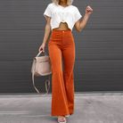 Frau in modischer, orangefarbener Schlaghose und weißem Strickoberteil, hält eine beige Handtasche. Trendige Damenmode, Herbstoutfit, Streetstyle.