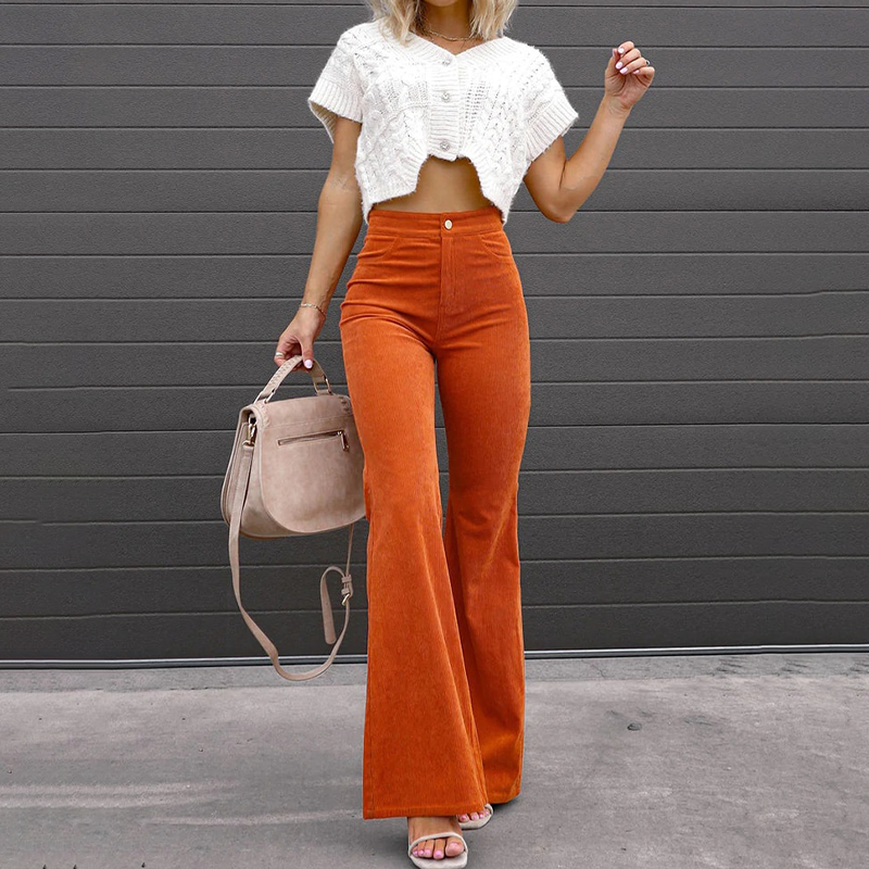 Frau in modischer, orangefarbener Schlaghose und weißem Strickoberteil, hält eine beige Handtasche. Trendige Damenmode, Herbstoutfit, Streetstyle.