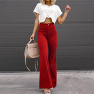 Frau in roter Schlaghose und weißem Strickoberteil, hält eine beige Handtasche. Modetrend, Damenmode, stilvolle Outfits, Herbstmode.