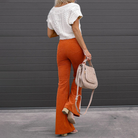 Frau in modischer, weißer Strickbluse und orangefarbener Schlaghose, hält beige Handtasche. Trendige Herbstmode, stilvolle Damenbekleidung.