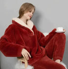 Frau in rotem Fleece-Pyjama mit weißem Kragen, entspannt auf Stuhl, hält Tasse. Gemütliche Wintermode, bequeme Nachtwäsche, stilvoller Komfort.