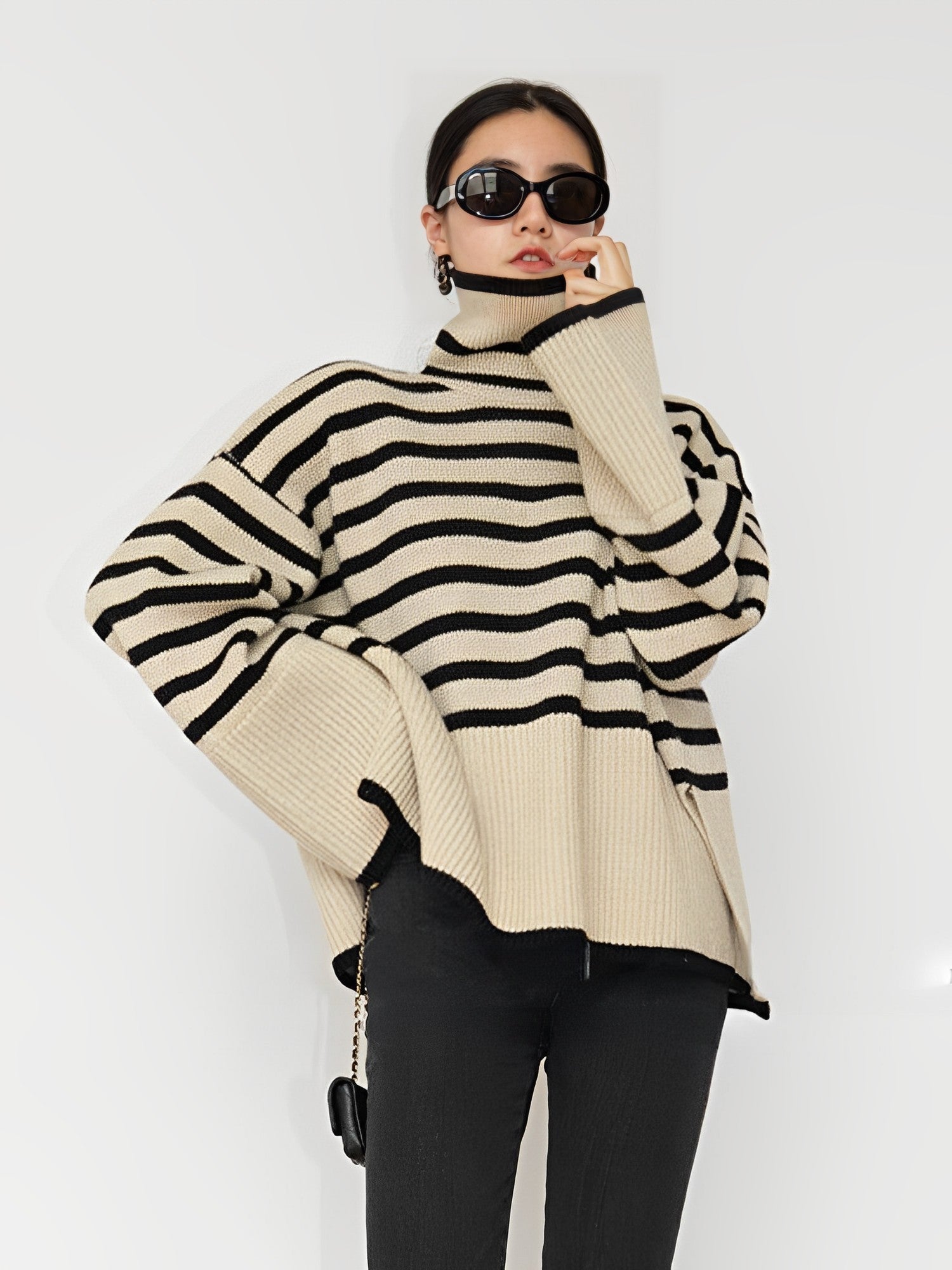 Gestreifter Rollkragenpullover in Beige und Schwarz, kombiniert mit schwarzer Hose und Sonnenbrille. Modetrend, Damenmode, Herbstoutfit.