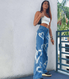 Frau in blauen Denim-Jeans mit Herz-Print, weißem Crop-Top und Sneakers. Trendige Mode, lässiger Look, ideal für Sommer und Freizeit.