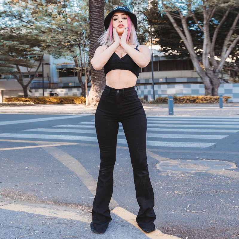 Frau in schwarzer Schlaghose und Crop-Top auf Straße, modisch mit Hut. Urbaner Stil, trendige Damenmode, Freizeitlook, Streetwear.