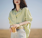Frau in hellgrüner Bluse und Jeans hält Kaffeebecher. Modetrend, Freizeitlook, Damenmode, stilvoll, lässig, Frühlingsoutfit, Outdoor.