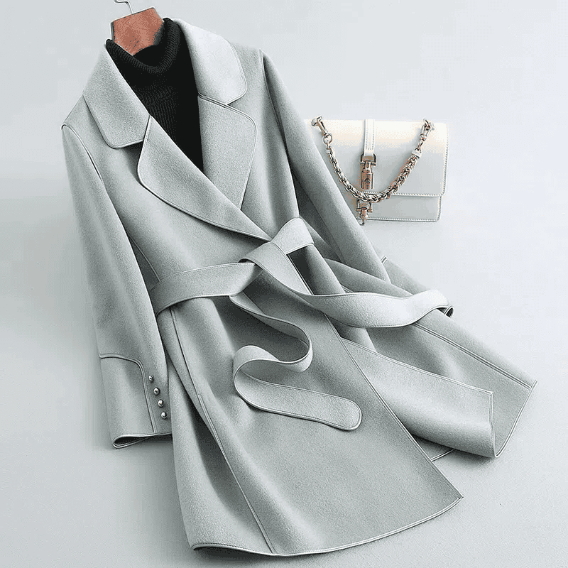 Eleganter grauer Damenmantel mit Gürtel, breitem Revers und Knopfleiste. Perfekt für Herbstmode. Inklusive stilvoller weißer Handtasche.