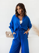 Frau in blauer Bluse und Hose, modisch elegant, mit beiger Handtasche. Perfekt für stilvolle Damenmode und Freizeitoutfits.