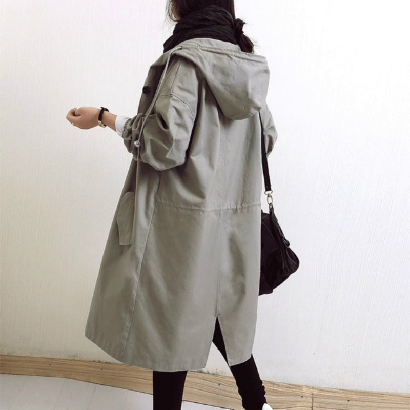 Damen-Trenchcoat in Grau mit Kapuze, lässiger Stil, ideal für Herbstmode. Perfekt kombinierbar mit schwarzer Tasche und Schal.