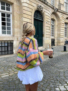 Frau in bunter Strickjacke und weißem Kleid hält Bubble Tea. Modetrend, Streetstyle, Herbstmode, Strickmode, Stadtspaziergang.