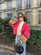 Frau in bunter Strickjacke, Jeans und Sonnenbrille vor historischer Fassade. Modetrend, Streetstyle, Herbstmode, lässiger Look.