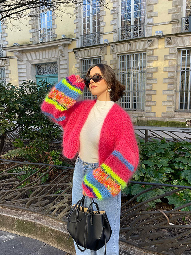 Frau in bunter Strickjacke, Jeans und Sonnenbrille vor historischer Fassade. Modetrend, Streetstyle, Herbstmode, lässiger Look.