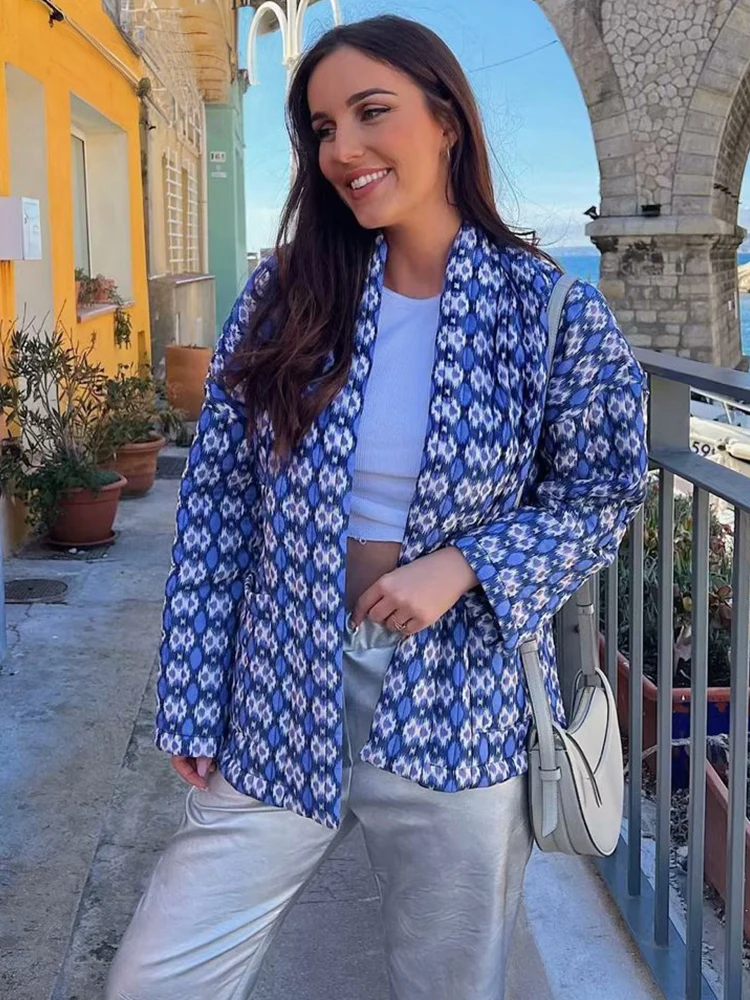 Frau in blauer, gemusterter Jacke und weißem Top, posiert lächelnd auf einer Terrasse. Modetrend, Damenmode, Freizeitlook, stilvoll.