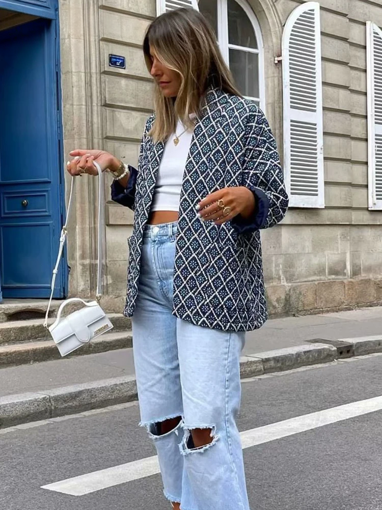 Frau in modischer Streetwear: gemusterter Blazer, weißes Crop-Top, zerrissene Jeans, kleine weiße Handtasche. Trendige Damenmode, urbaner Stil.