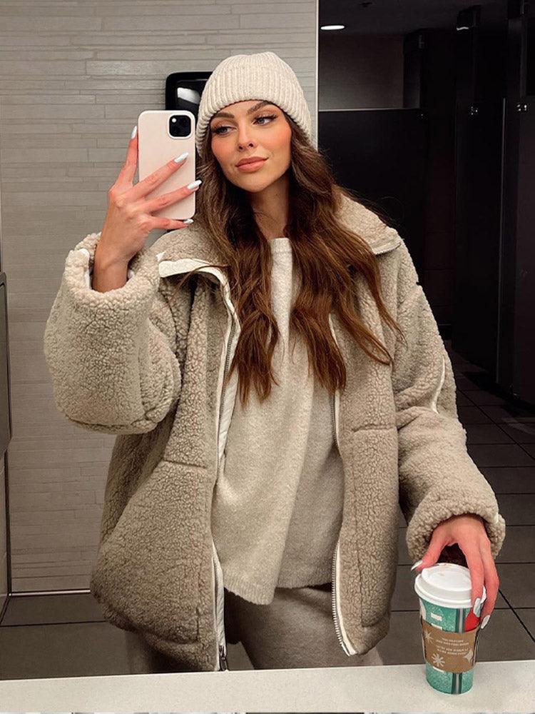 Frau in beiger Teddyjacke und Mütze macht Selfie im Spiegel, hält Starbucks-Becher. Wintermode, gemütlicher Look, Streetstyle-Trend.