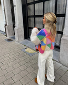 Frau in bunter Strickjacke mit geometrischem Muster, weiße Hose, braune Schuhe. Modetrend, Streetstyle, Herbstmode, Damenbekleidung.