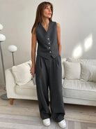 Frau in grauem Anzug mit Weste und Hose, moderne Wohnzimmer-Einrichtung, stilvolle Mode.