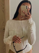 Frau in weißem, geripptem Langarmshirt macht Selfie mit Smartphone, hält Sonnenbrille. Modetrend, Damenmode, Selfie, Accessoires.