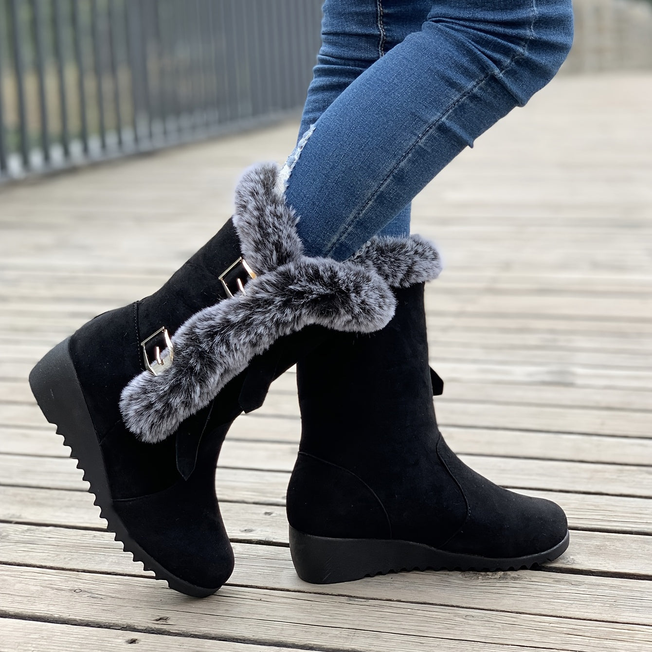 Schwarze Winterstiefel mit Kunstfellbesatz, Keilabsatz und Schnallen, getragen auf Holzsteg. Modische Damenstiefel, warm und stilvoll.