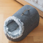 Graues Katzenbett aus Filz mit Plüschrand auf Holzboden, gemütlich und tragbar.