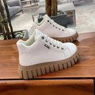Weiße Sneaker mit dicker, geriffelter Sohle auf Holztisch. Modische, bequeme Schuhe für Damen und Herren. Ideal für Freizeit und Alltag.
