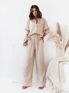 Elegantes Damen-Outfit in Beige: Weite Hose und lockere Bluse aus Leinen, ideal für Sommermode. Perfekt kombiniert mit Sandalen und Strohtasche.