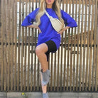 Frau in blauem Sportset mit Gürtel, schwarze Shorts, graue Stiefeletten. Trendige Freizeitmode, ideal für sportliche und lässige Outfits.