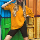 Frau in orangefarbenem T-Shirt und schwarzen Radlerhosen vor bunter Wand. Modetrend, Freizeitkleidung, sportlich, urbaner Stil.