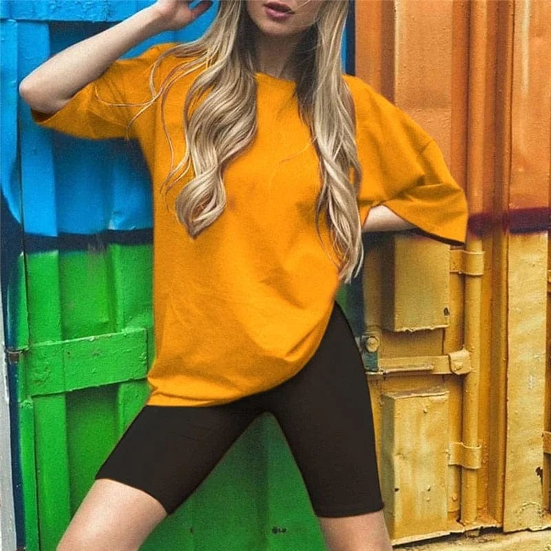 Frau in orangefarbenem T-Shirt und schwarzen Radlerhosen vor bunter Wand. Modetrend, Freizeitkleidung, sportlich, urbaner Stil.