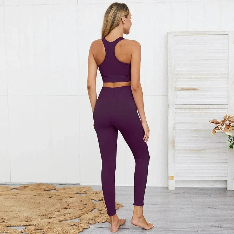 Frau in lila Sportset, bestehend aus Leggings und Sport-BH, steht in modernem Raum. Fitnessmode, bequeme Sportbekleidung, athletischer Look.