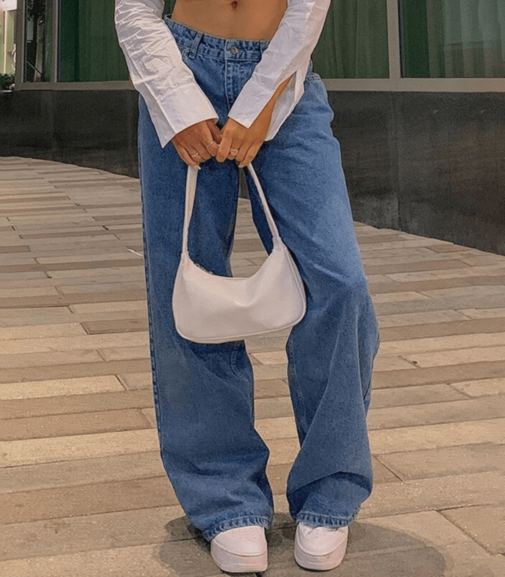 Einfarbige Baggy-Jeans mit niedriger Taille, kombiniert mit weißem Crop-Top und Handtasche. Trendige Damenmode, lässiger Streetstyle.