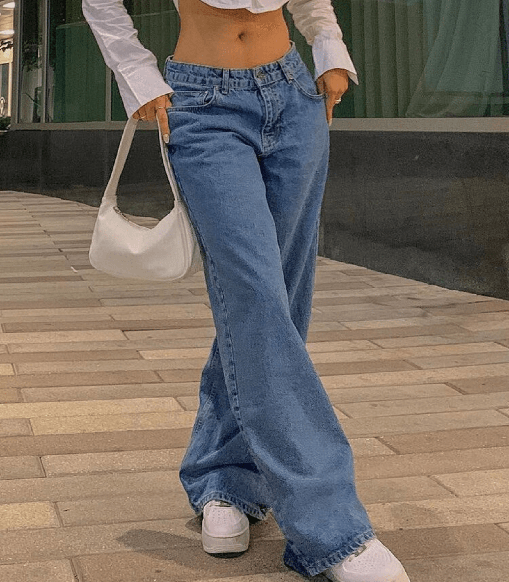 Einfarbige Baggy-Jeans mit niedriger Taille, kombiniert mit weißem Crop-Top und Tasche. Trendige Damenmode, lässiger Streetstyle-Look.