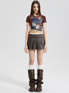 Frau in modischem Outfit: bedrucktes Crop-Top, brauner Minirock, hohe Stiefel. Trendige Damenmode, urbaner Stil, Streetwear-Look.