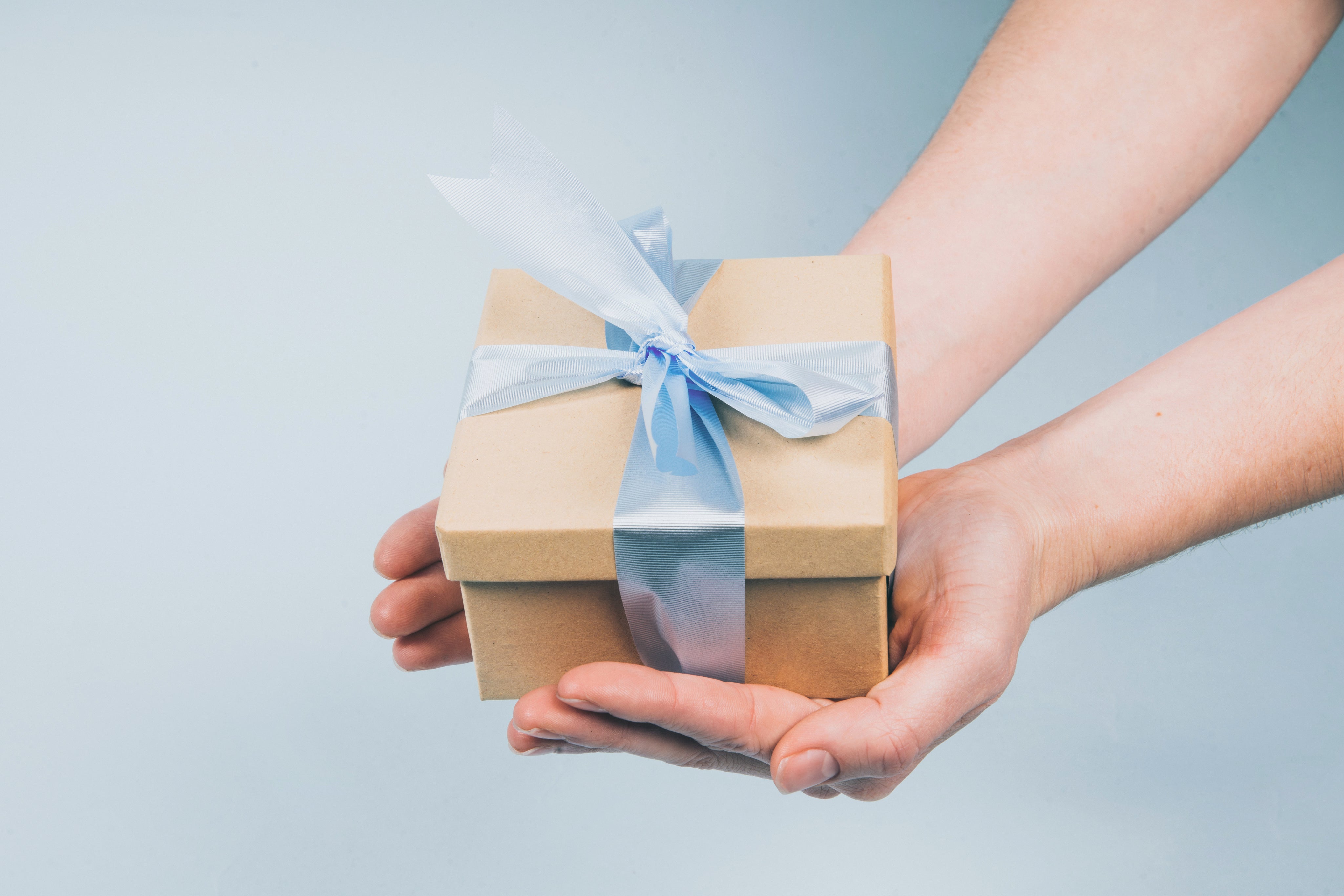 Geschenkbox in Hand mit blauem Band, ideal für besondere Anlässe. Perfektes Präsent, stilvoll verpackt, hochwertig und elegant.