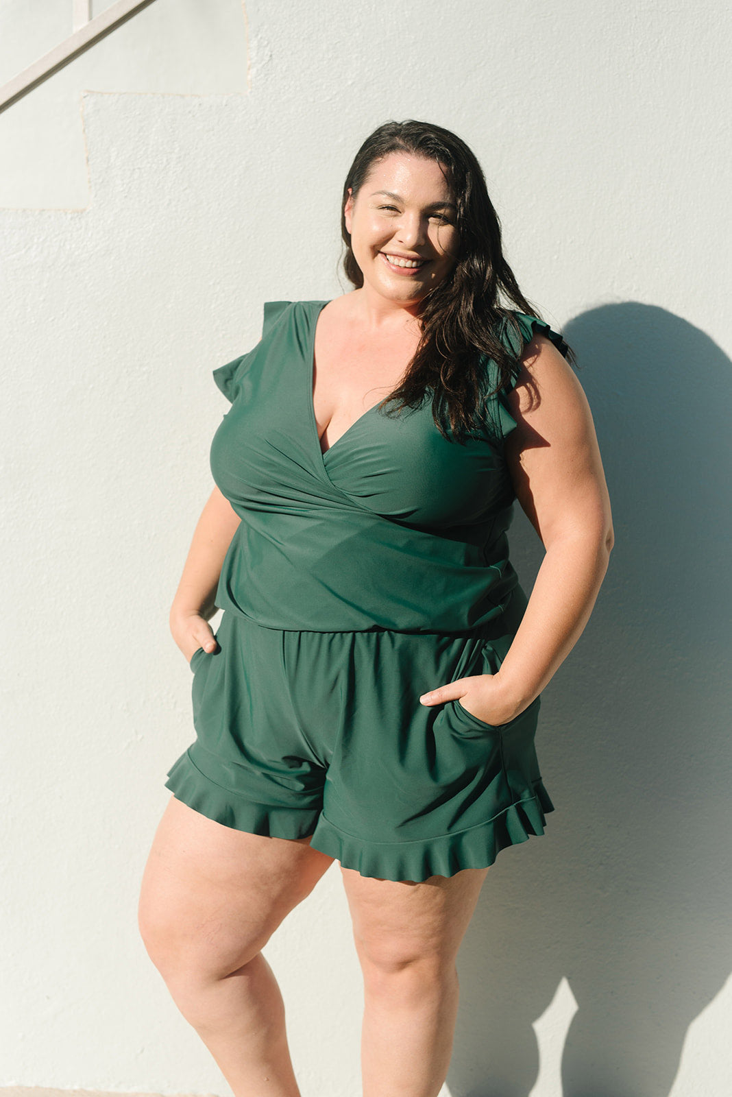 Frau in grünem Badeanzug mit Rüschen, Sommermode, Plus-Size, draußen, lächelnd.
