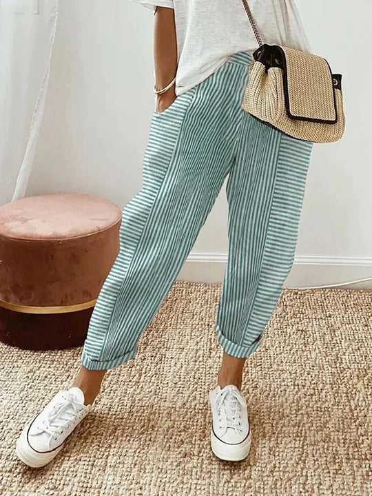 Damenhose mit grün-weißen Streifen, kombiniert mit weißem T-Shirt und Strohtasche. Perfekt für lässige Sommermode und Freizeitoutfits.