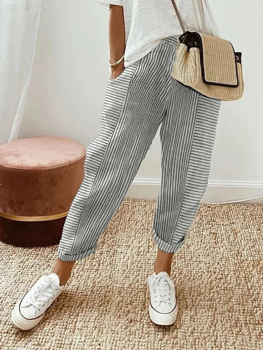 Gestreifte Damenhose in Grau-Weiß, kombiniert mit weißen Sneakers und einer beigen Umhängetasche. Perfekt für lässige Sommeroutfits.